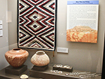 <p>Old Chocolate and Other Surprises: Learning from the May Collection<br />Case 1. More Than Just Pretty: Forensic Research in the May Collection. This exhibit explores the potential for items from the David W. May Collection to yield information through various types of research. Seen in this case is (1) a small Ganado style Navajo rug, hand woven ca. 1995; (2) a large Jemez sgraffito jar made by Alvina Yepa in 2002. It was a prize winner at the 2002 American Indian Celebration held at USD; (3) a large Hohokam red-on-buff jar made ca. C.E. 1275, from the Phoenix and Tucson basins in Arizona; and (4, 5, 6) examples of shell jewelry, a glycynmeris bracelet, and a conus tinkler from the Southwest, and a hand carved shell gorget made by Cree/Cherokee artist Dan Townsend from Florida.</p><p style="text-align: right;"><em>Photograph by Erika Johnson.</em></p>