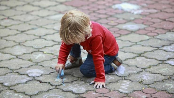 Little kid in red sweater coloring with chalk on the ground