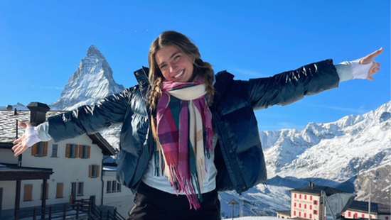 Young blonde woman posing in front of the Matterhorn with her arms raised high wearing winter clothing