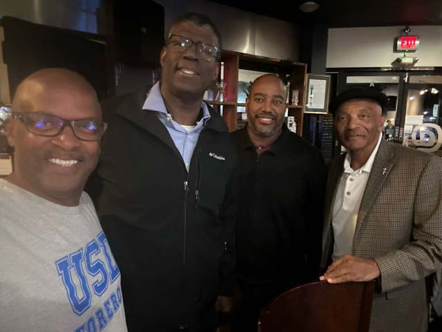 Four black alumni hanging out. One of them is rocking a dapper hat.