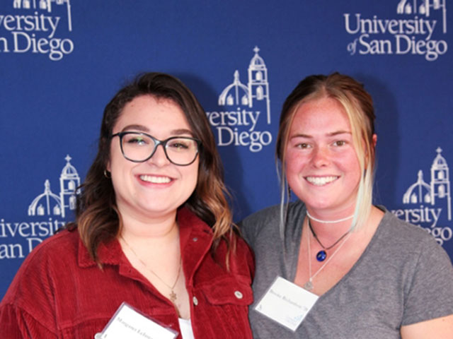Two female students smiling in front of blue backdrop