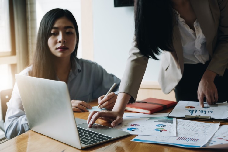 Women sit at desk in front of laptop reviewing financial data