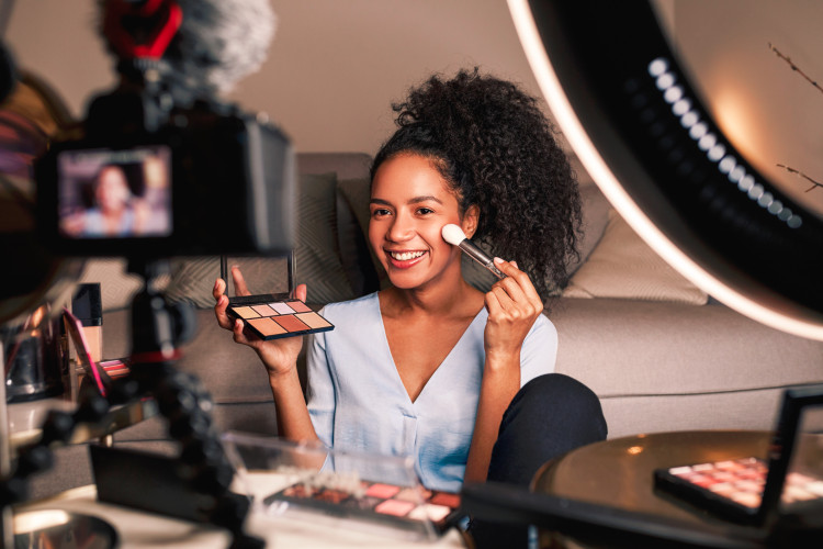 A beauty blogger puts on makeup in front of a camera.