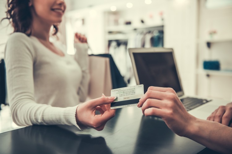 Cashier hands credit card to shopper holding shopping bag.