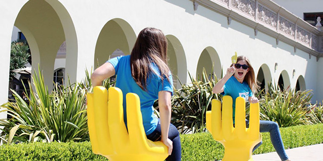 Students sitting in hand-shaped chairs outside