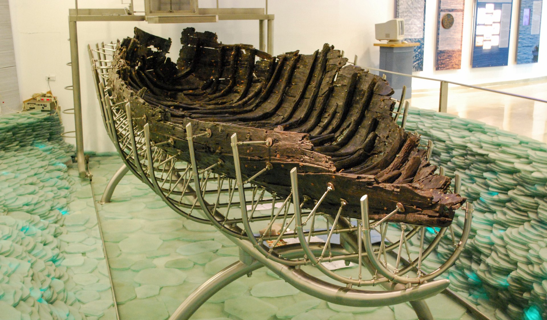 A preserved ancient wooden boat displayed in a museum, supported by a modern metal frame for stabilization.