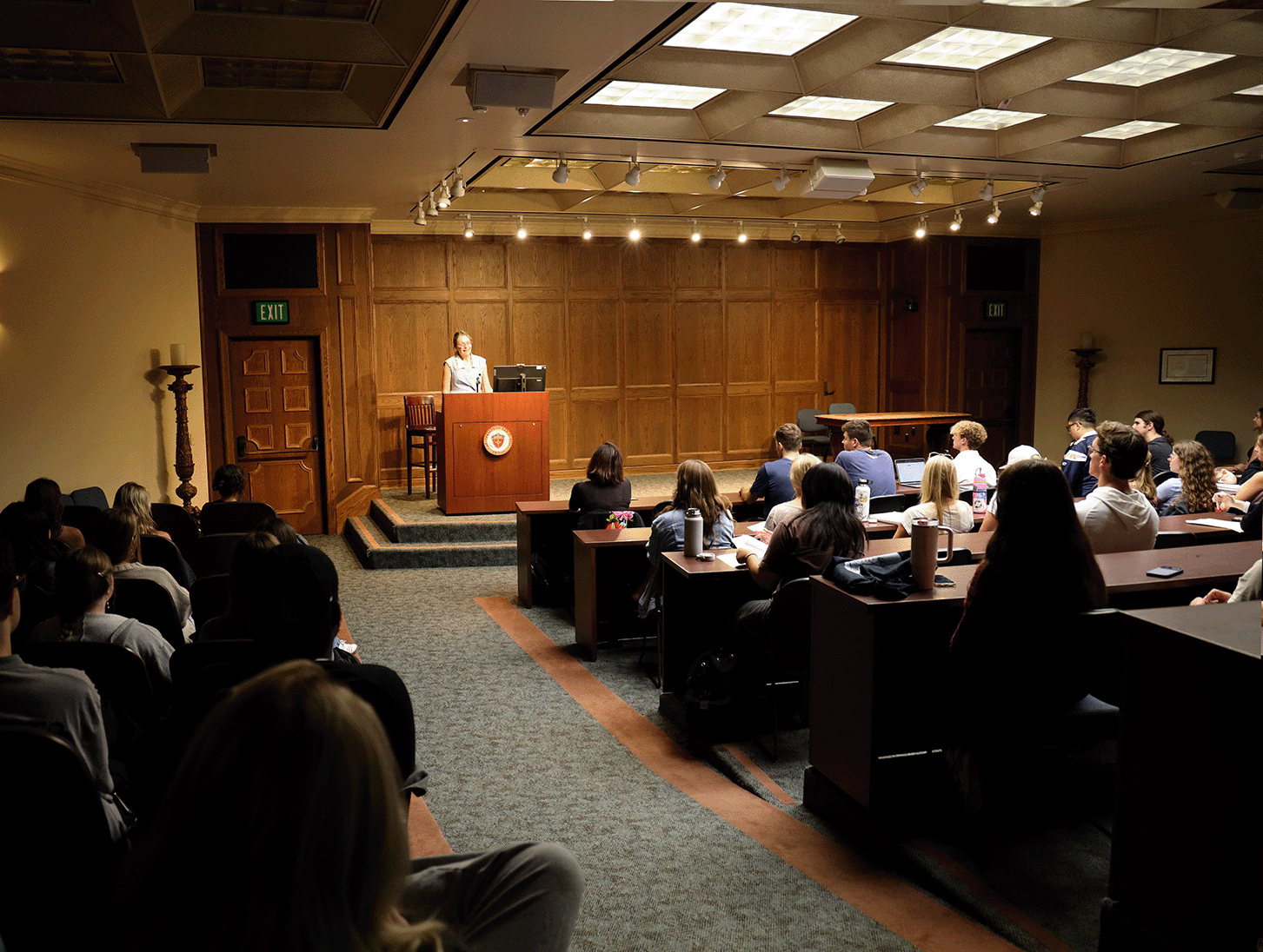 A speaker at a podium on the Manchester Auditorium stage with people in the audience.