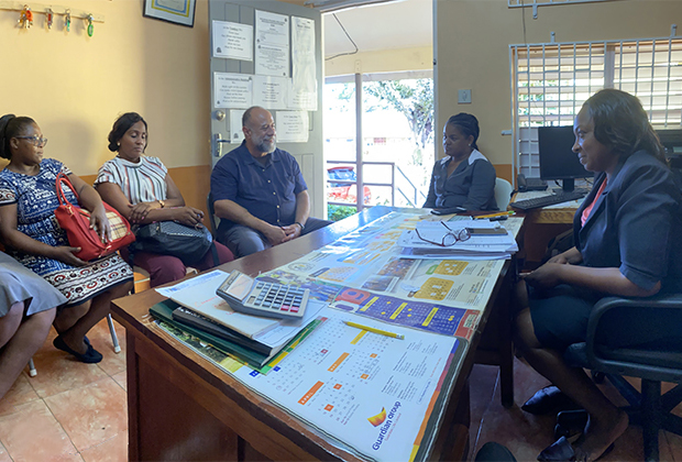 5 people sit together in a Jamaican classroom discussing community engagement ideas.