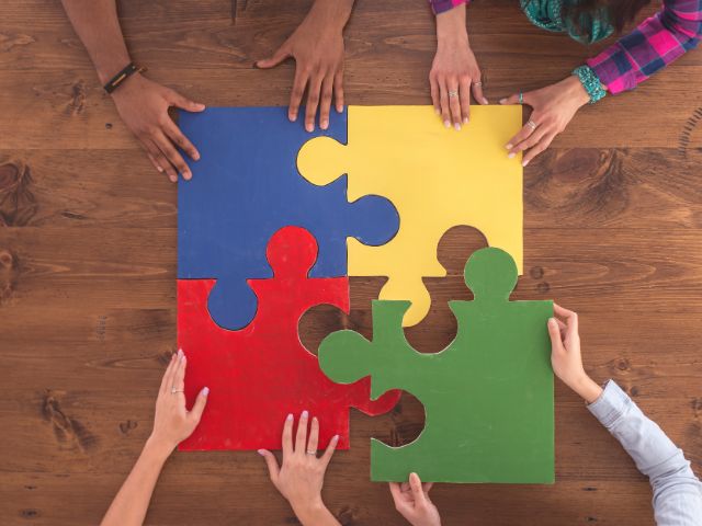 Four people putting together four different colored large puzzle pieces.
