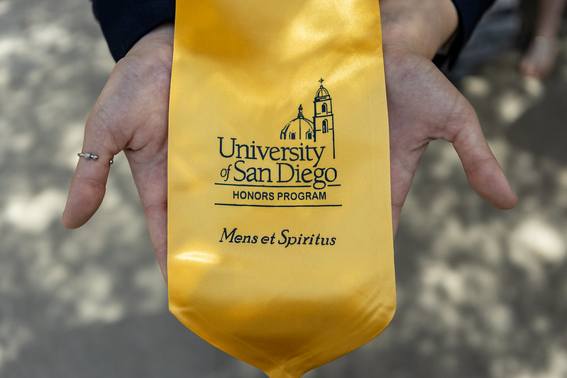 Two hands holding out the gold Honors graduation stole.