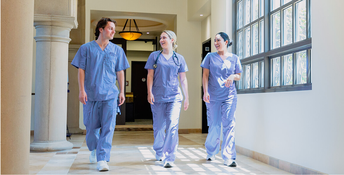 group of nursing students in blue scrubs walking in hallway