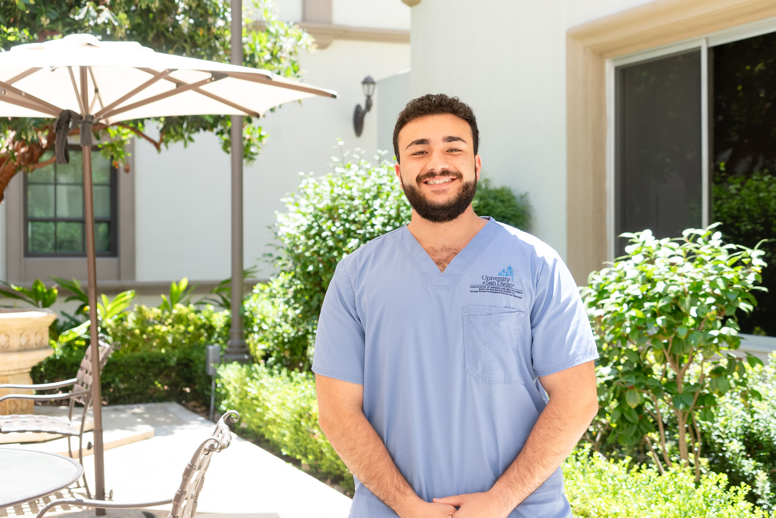 Male MEPN student wearing blue scrubs standing in BINR patio smiling at camera