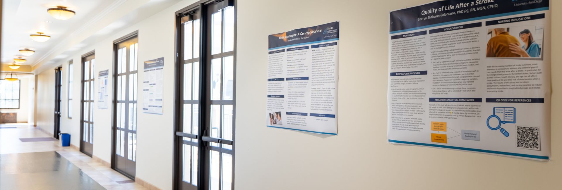 Academic research posters hang on a white wall in a sunlit hallway at the USD Hahn School of Nursing