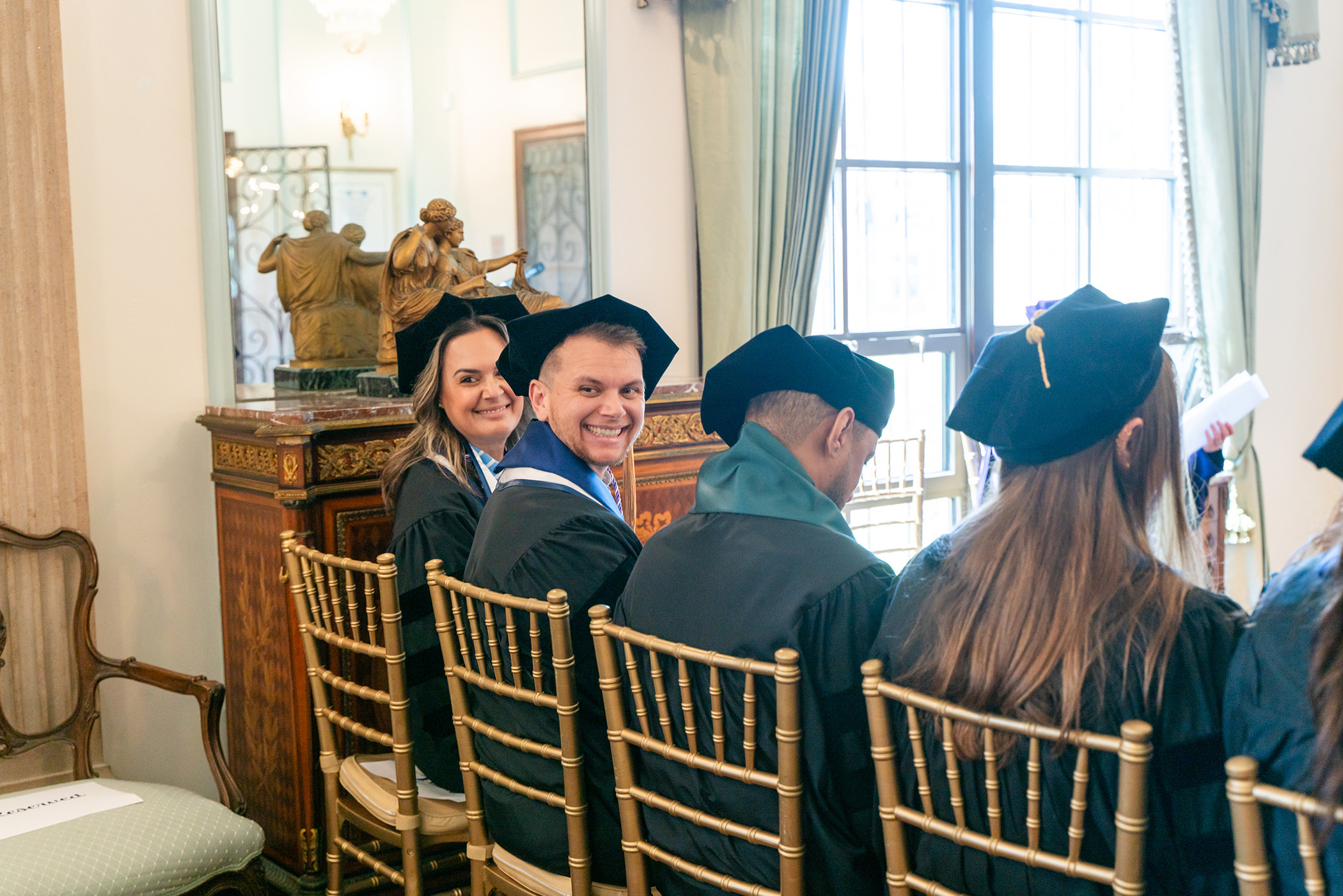 Two PhD graduates smile at crowd behind them during PhD hooding ceremony