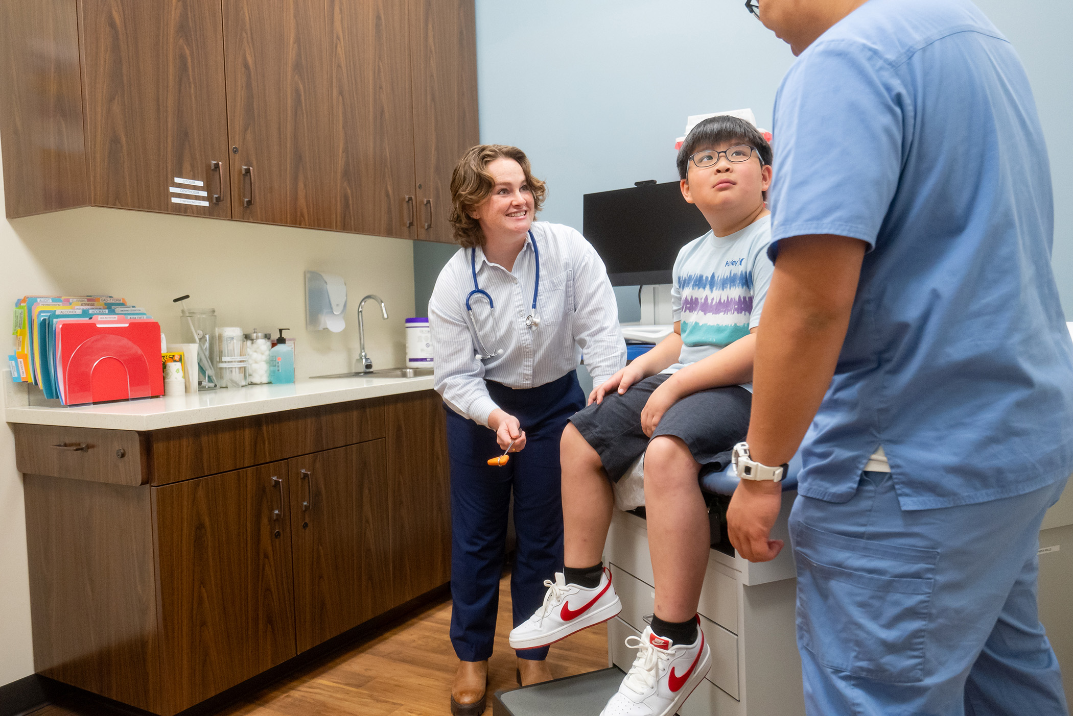 fnp student examines boy's reflexes as he looks up at RN in blue scrubs