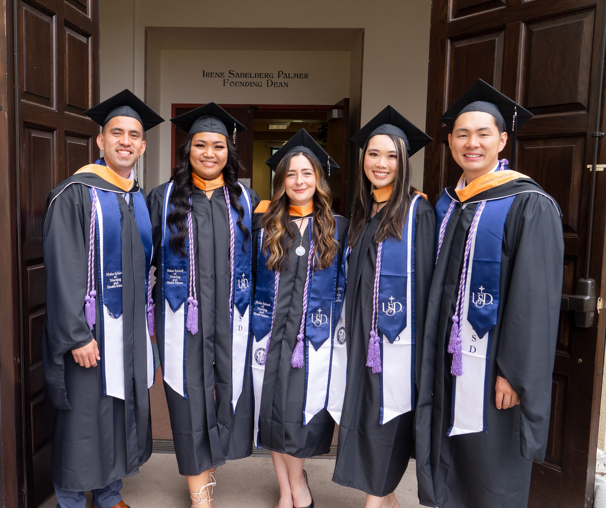 diverse group of MEPN students in graduation regalia standing in doorway