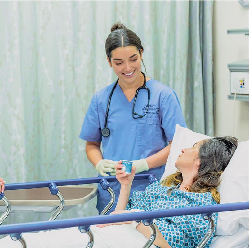 Nursing student in blue scrubs at beside next to hospital patient