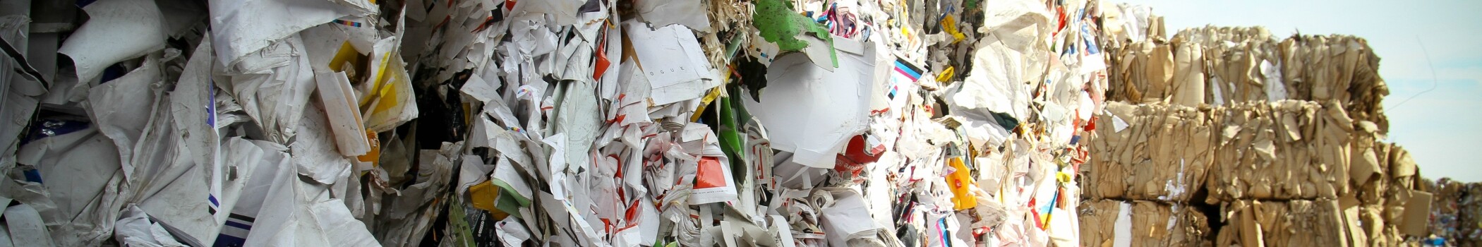 Close-up of mixed paper and plastic waste piled together, showing crumpled packaging, shredded materials, and debris in a recycling or landfill setting.