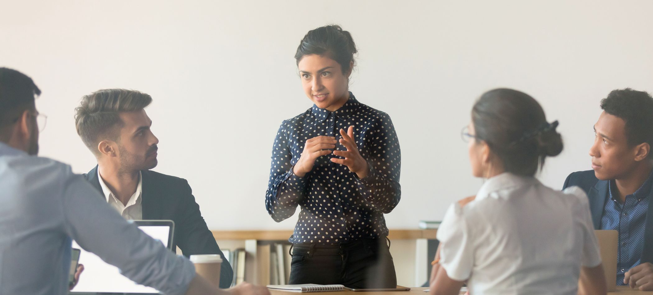 lady standing in front of sitting coworkers talking