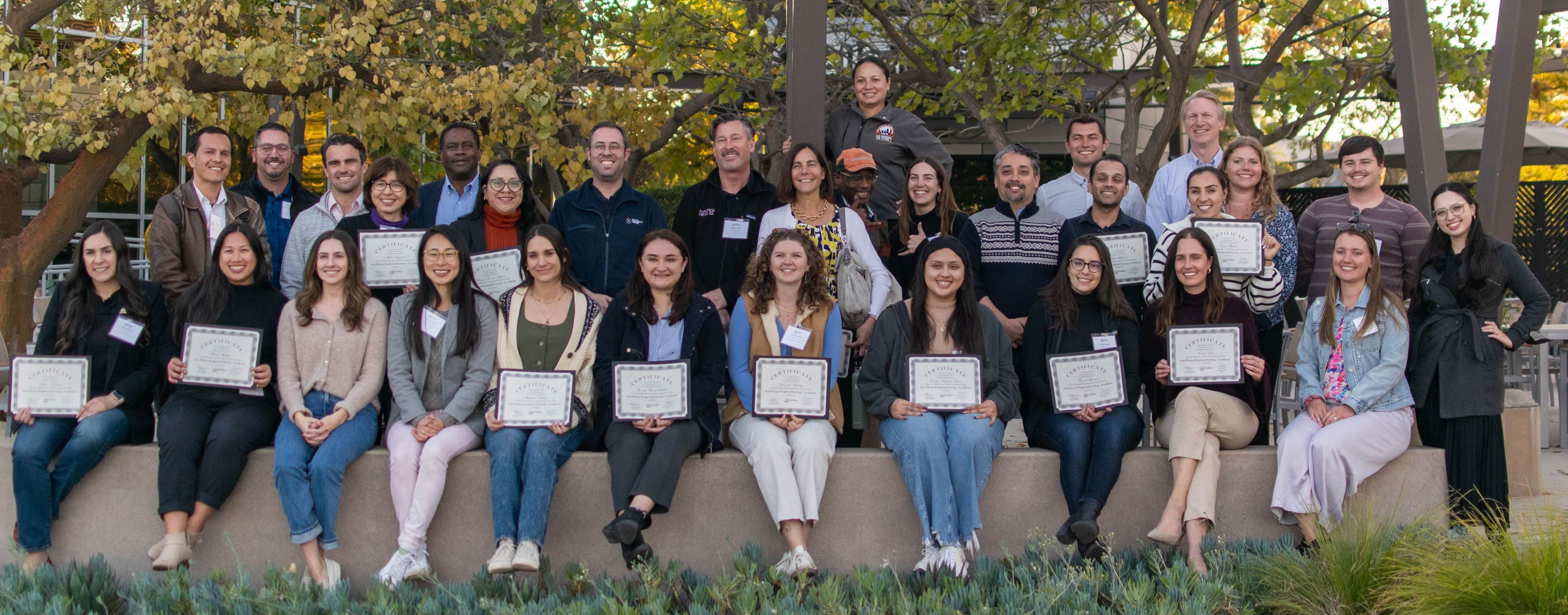 Energy Academy Cohort 1 sitting outside smiling, some with certificates of comp