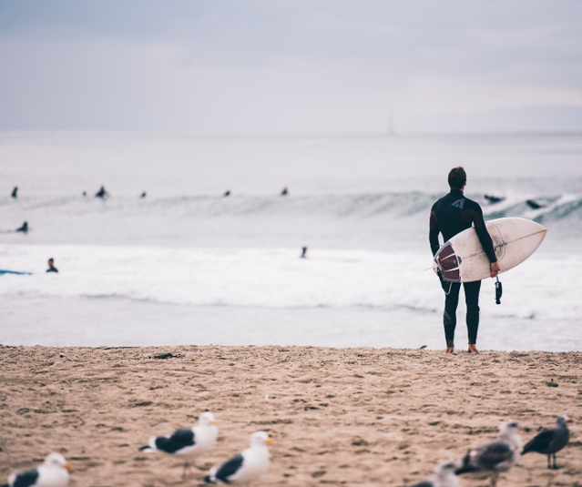 A surfer looking at the ocean from the beach