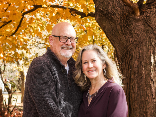 Bob and Darci O'Connell stand smiling in front of a leafy background.