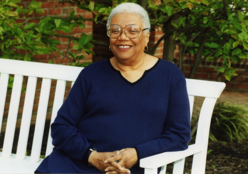 Lucille Clifton sitting on a bench outside with her hands clasped on her lap