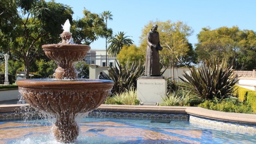 Water emerges from fountain on University of San Diego campus with a statue of a priest in the background