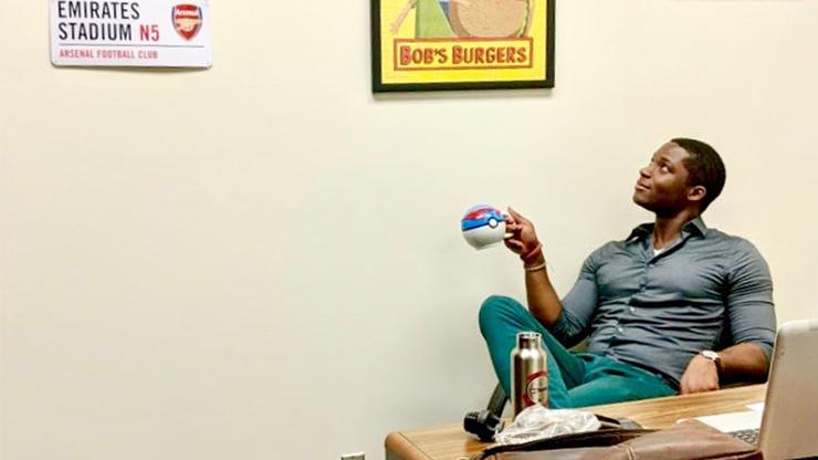 USD School of Business Assistant Professor of Economics Jason Campbell sits in his office chair looking up at his memorabilia of FC Barcelona soccer gear and Bob's Burgers poster
