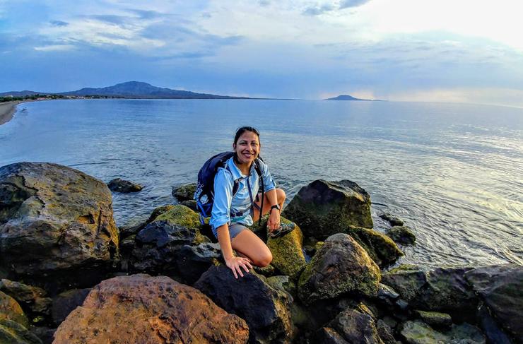 Anai sits on some rocks by the beach.