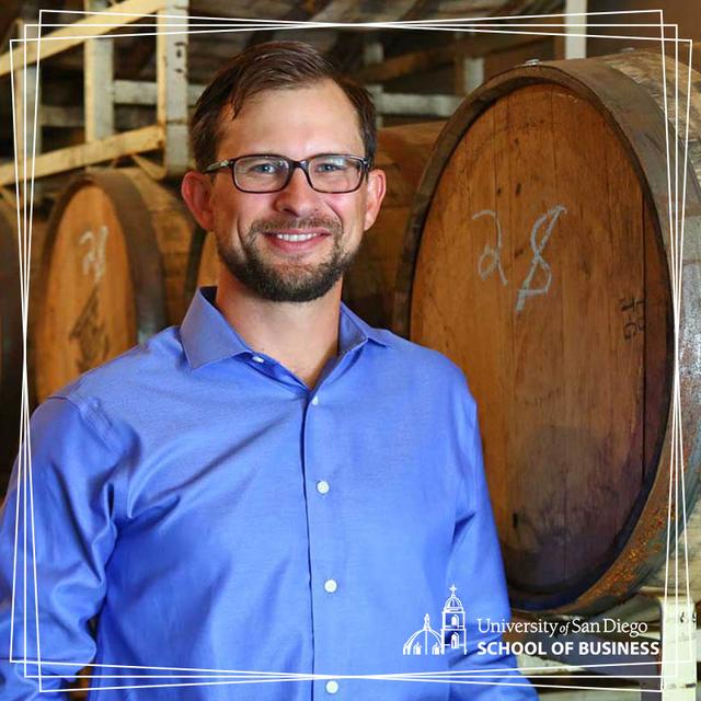 USD alumnus, Bryan Carpenter, BAC '07 posing in front of beer barrels