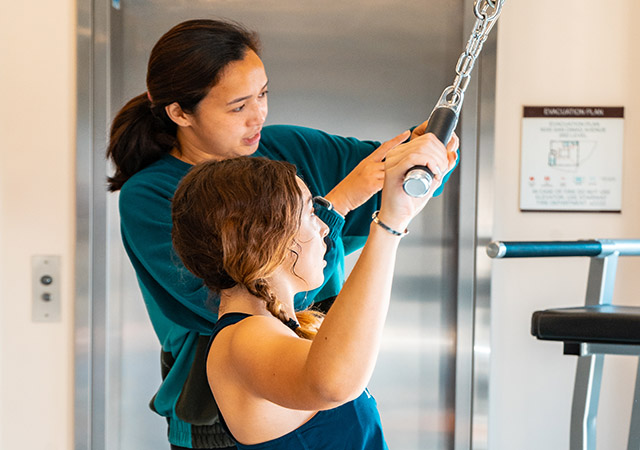 Personal trainer Madel is helping a student with a workout machine.