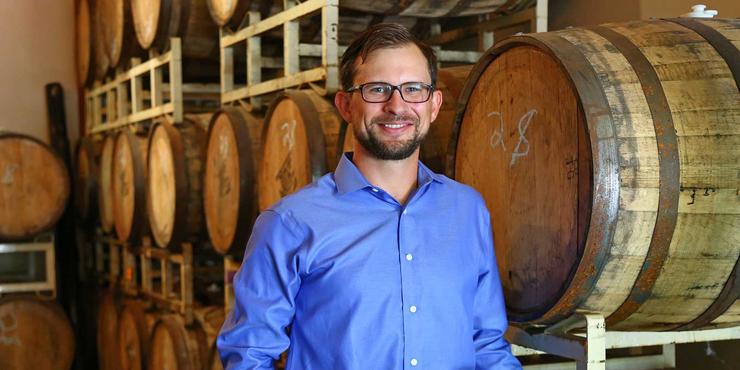USD alumnus, Bryan Carpenter, BAC '07 posing in front of beer barrels