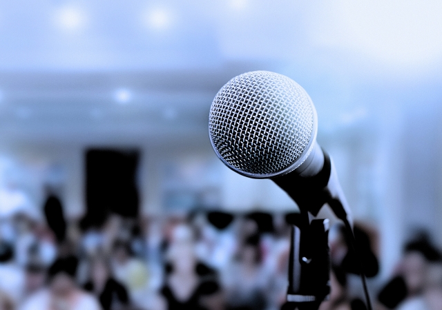 This is a picture of a standing microphone in the foreground with a crowd in the background. 