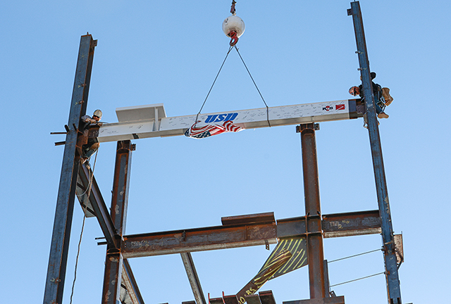 Two construction workers work together to secure a historic beam into place atop the frame of USD's  new Wellness Center and Basketball Practice Facility during a topping off ceremony on Monday, Jan. 29, 2024. Photo by Matthew Piechalak