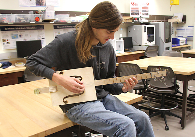Engineering student strums a cigar-box shaped guitar that he made in an Acoustics of Musical Instruments course.