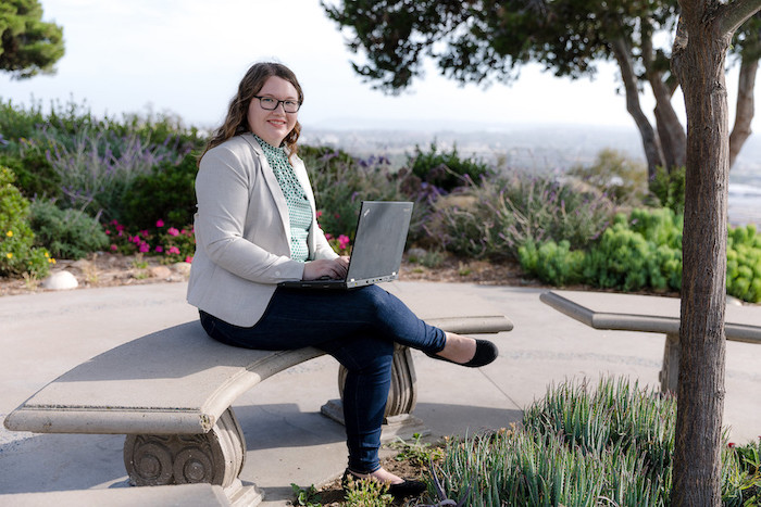 A university of san diego school of business student sits on campus with her laptop