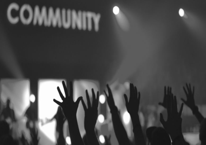 black and white photo of crowd of people reaching out to a sign that reads community
