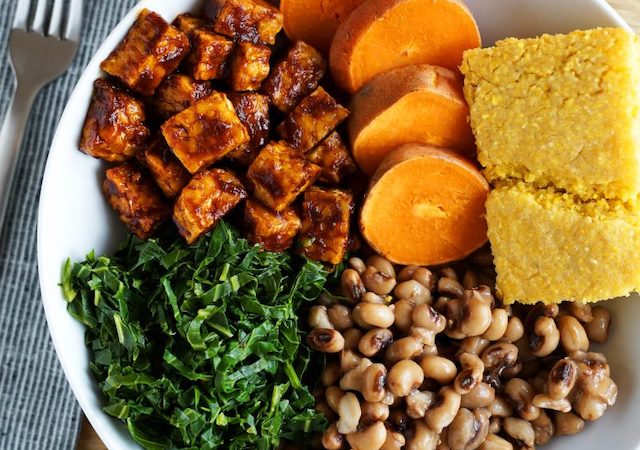 Fork next to a plate of vegan soul food, including greens, beans, yams, bread, and more.