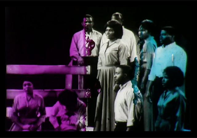 Video still from An Ecstatic Experience. Purple, white and blue washed over a black and white image of a black actors on stage.