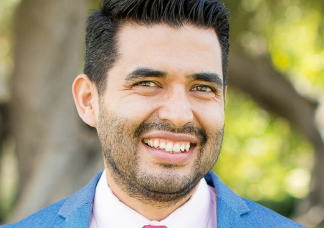 headshot of Rodrigo, wearing a light blue suit and standing outside in front of a tree