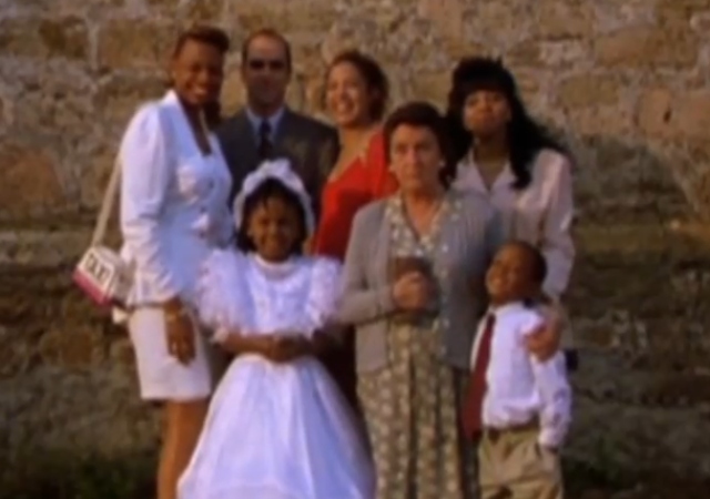 A group of what looks like a Spanish multiracial family celebrating a first communion, including two black women, a young black girl, a little black boy, a white/Spanish older woman, a middle age whit