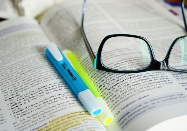 open book with glasses, highliter and pen atop