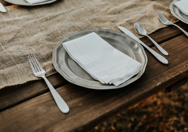 a wooden table with an empty place setting of a silver plate and utensils