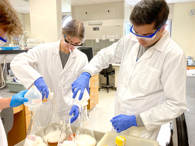 Students in lab pouring liquid into scientific flasks