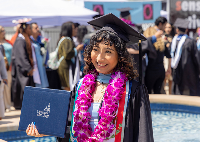 A graduate holds her degree outside the Jenny Craig Pavilion