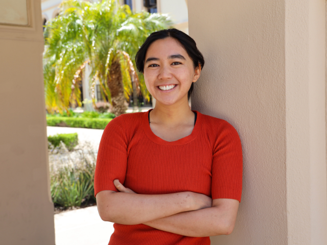 Omsu Nguyen poses for a photo on USD campus, smiling with her arms folded.