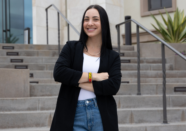 Donatella Falcomer stands in front of a staircase at the Knauss Center for Business Education with her arms crossed wearing a black blazer and Eswatini.