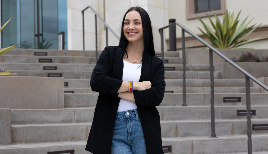 Donatella Falcomer stands in front of a staircase at the Knauss Center for Business Education with her arms crossed wearing a black blazer and Eswatini.