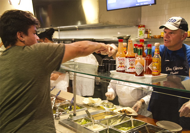 President Harris and a student exchange a friendly fist bump prior to the former putting together the student's burrito while in line at Pavilion Dining's Maiz food station.